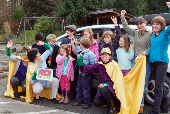 OPALCO Energy Services staff (in capes from left): Beth Anderson, Elisa Howard and Anne Bertino recognize students and teachers from Shaw Island School for their energy efficiency calendar.