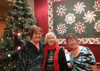 Marcia Gillingham, Joyce Green and Mary Greenwell , (with a baby in the cradle behind them) welcome all to the Holiday Festival of the Arts at the Senior Center 2013